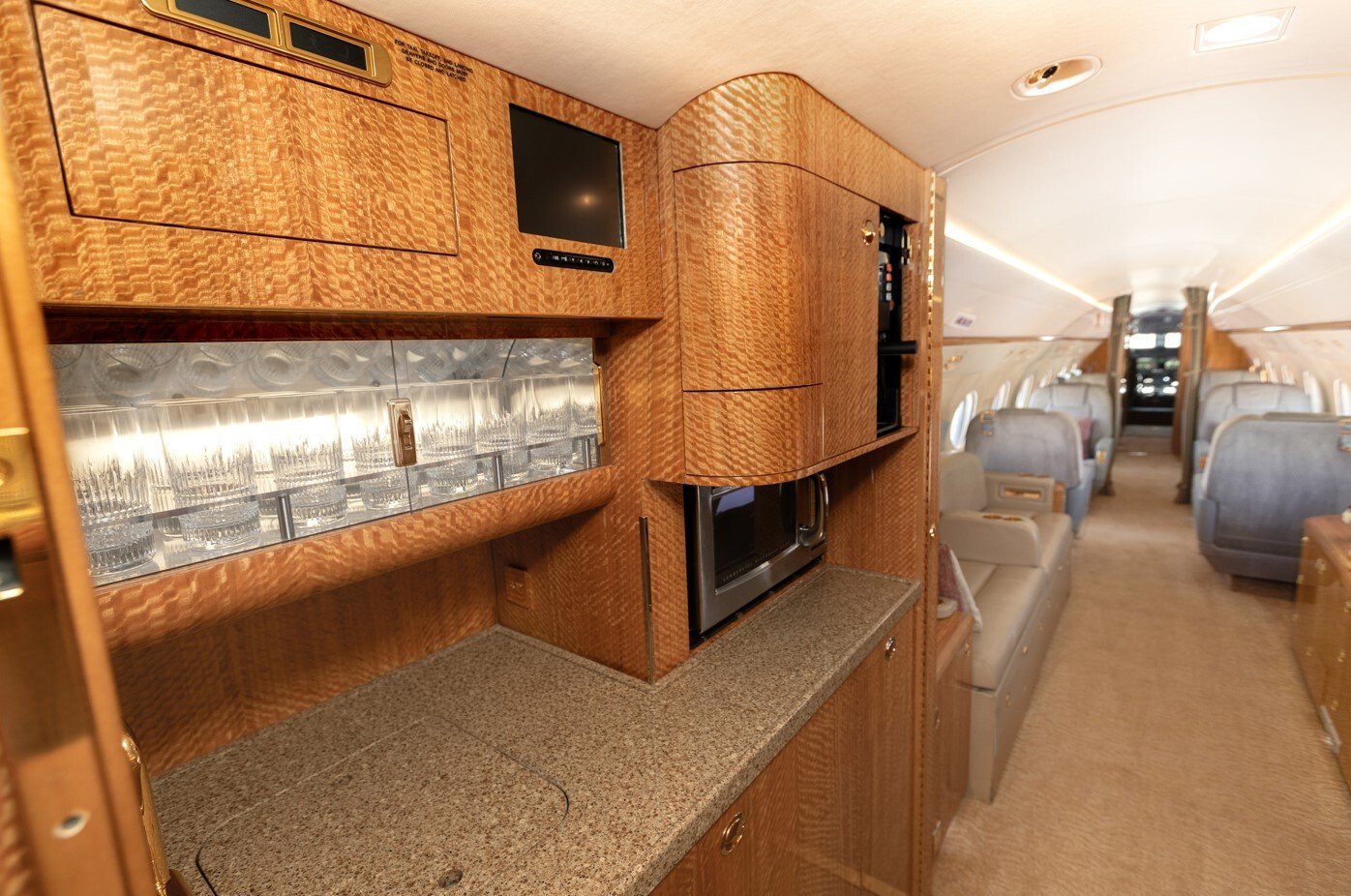 The aft galley of this 2010 Gulfstream G550 is elegantly designed with fine wood cabinetry, a polished stone countertop, and premium appliances including a microwave and ample storage. Crystal glassware and refined finishes highlight the jet’s commitment to luxury and convenience, ensuring seamless in-flight service for passengers.