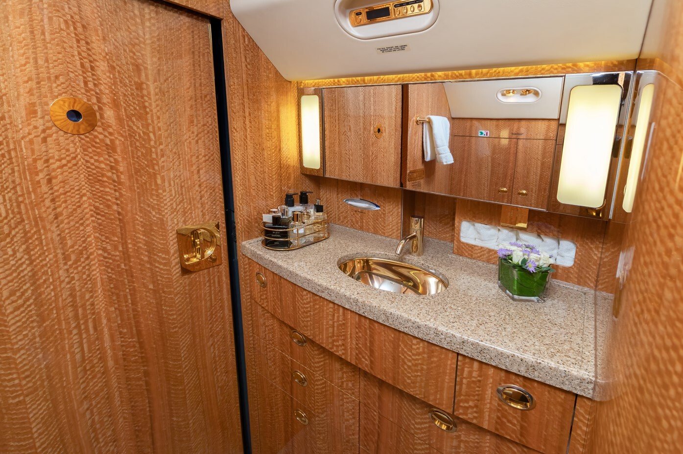 The aft lavatory of this 2010 Gulfstream G550 exudes refined craftsmanship, featuring rich wood cabinetry, a polished stone countertop, and gold-plated fixtures. Thoughtful lighting, ample storage, and elegant accents create a luxurious and functional space for comfort and privacy during flight.