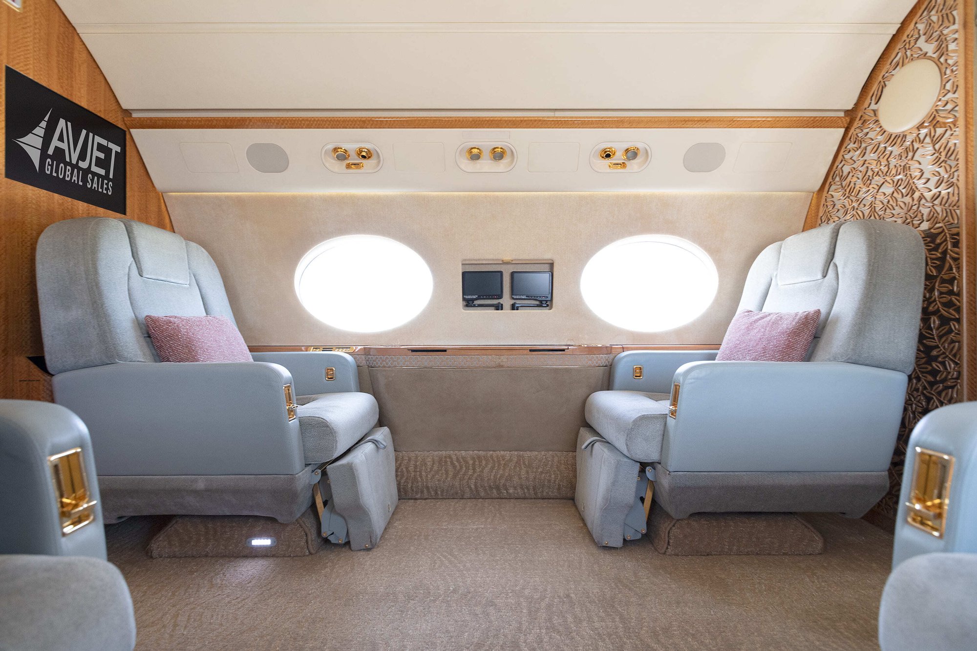 The forward cabin of this 2010 Gulfstream G550 features a luxurious four-seat club configuration with wide, reclining leather seats accented by soft throw pillows and gold hardware. Elegant wood paneling and large oval windows create a bright, refined environment ideal for productivity or relaxation.