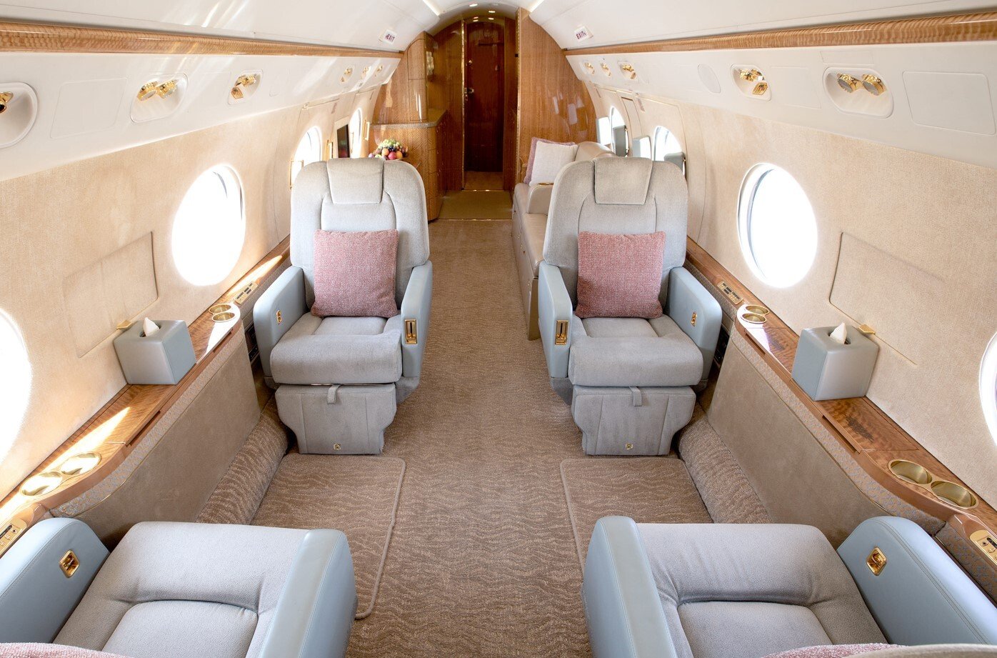 The mid cabin of this 2010 Gulfstream G550 features a refined four-seat club arrangement with luxurious leather recliners, accented by polished wood surfaces and gold details. Large oval windows fill the space with natural light, while soft tones and plush materials create a welcoming environment for relaxation or conversation.