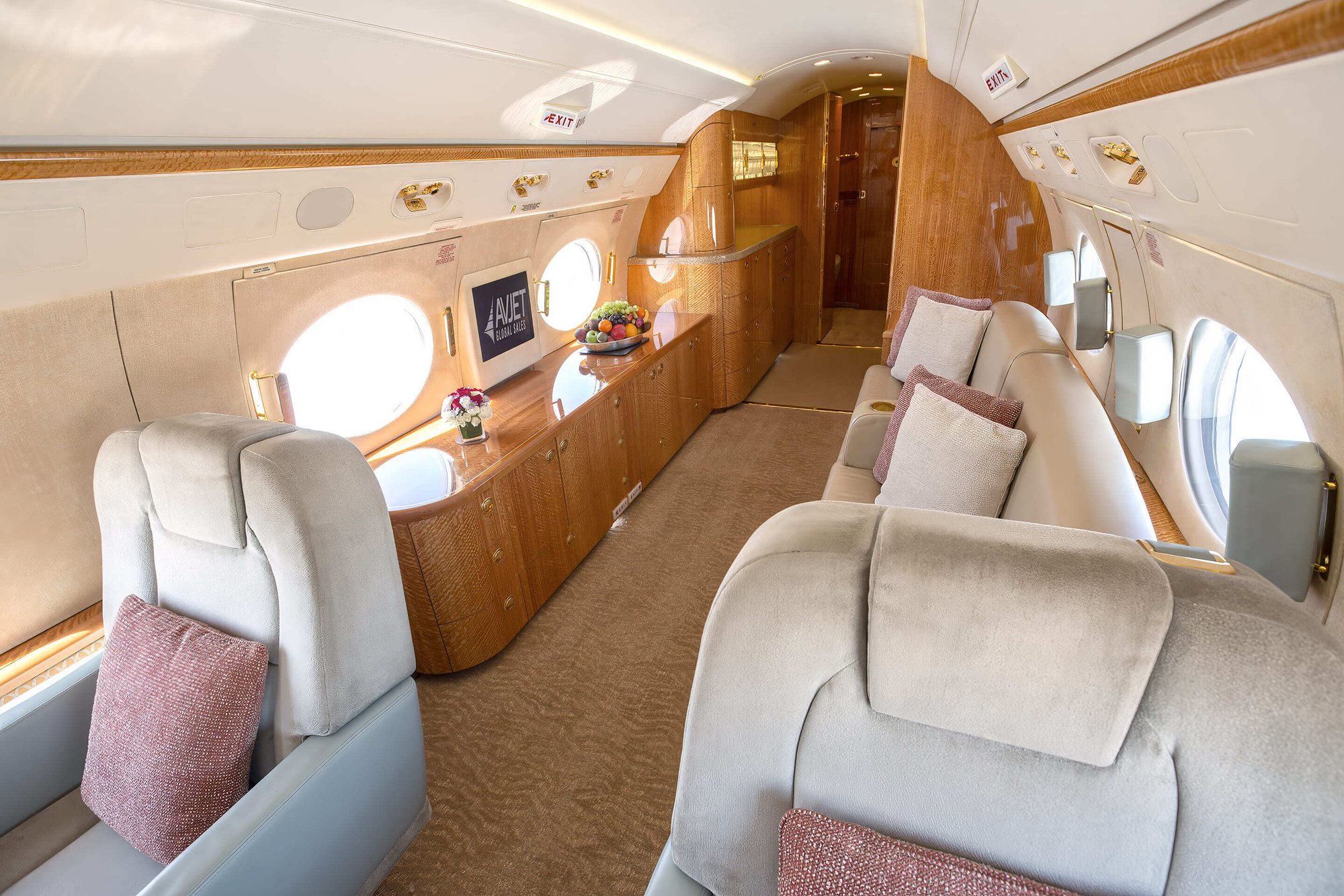 The aft cabin of this 2010 Gulfstream G550 offers a relaxing lounge area featuring a spacious divan opposite two plush club seats. Warm wood finishes, soft beige tones, and large oval windows create an inviting atmosphere filled with natural light — ideal for unwinding or converting into a private sleeping area during long-range flights.