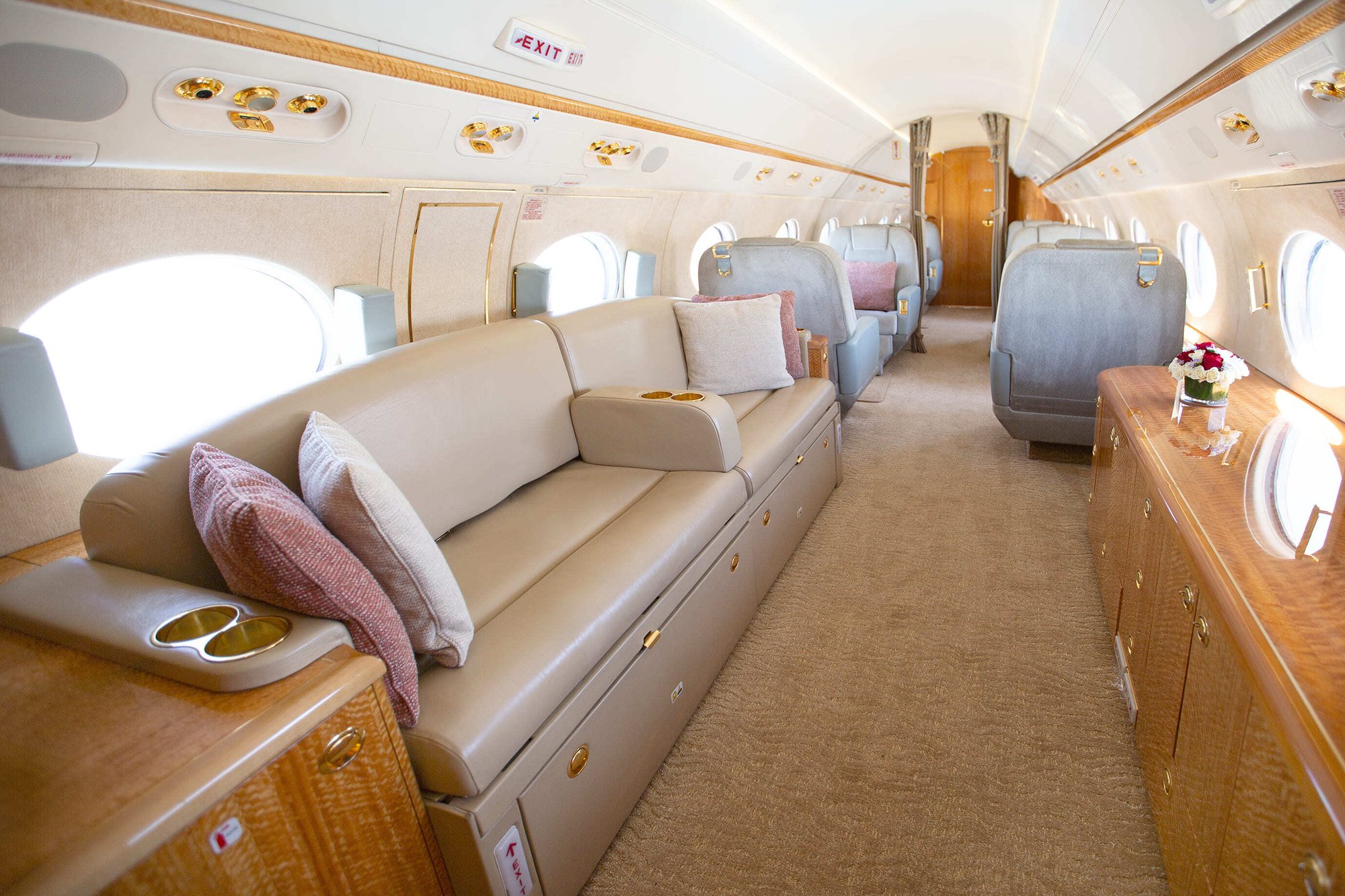 The aft cabin of this 2010 Gulfstream G550 features a spacious three-place divan opposite two plush club seats, blending comfort and elegance. Warm neutral tones, fine wood finishes, and gold-accented details create a luxurious atmosphere, while large windows provide abundant natural light and an open, inviting feel.