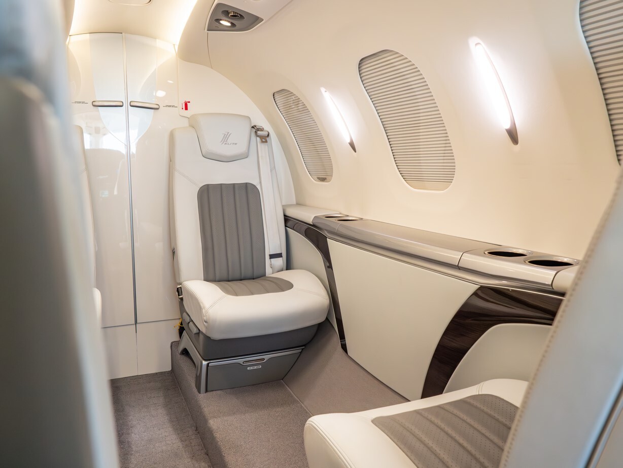 2022 HondaJet Elite S aft cabin interior featuring an individual executive leather seat, side console with cup holders, window shades, and refined LED lighting in a quiet light business jet cabin.