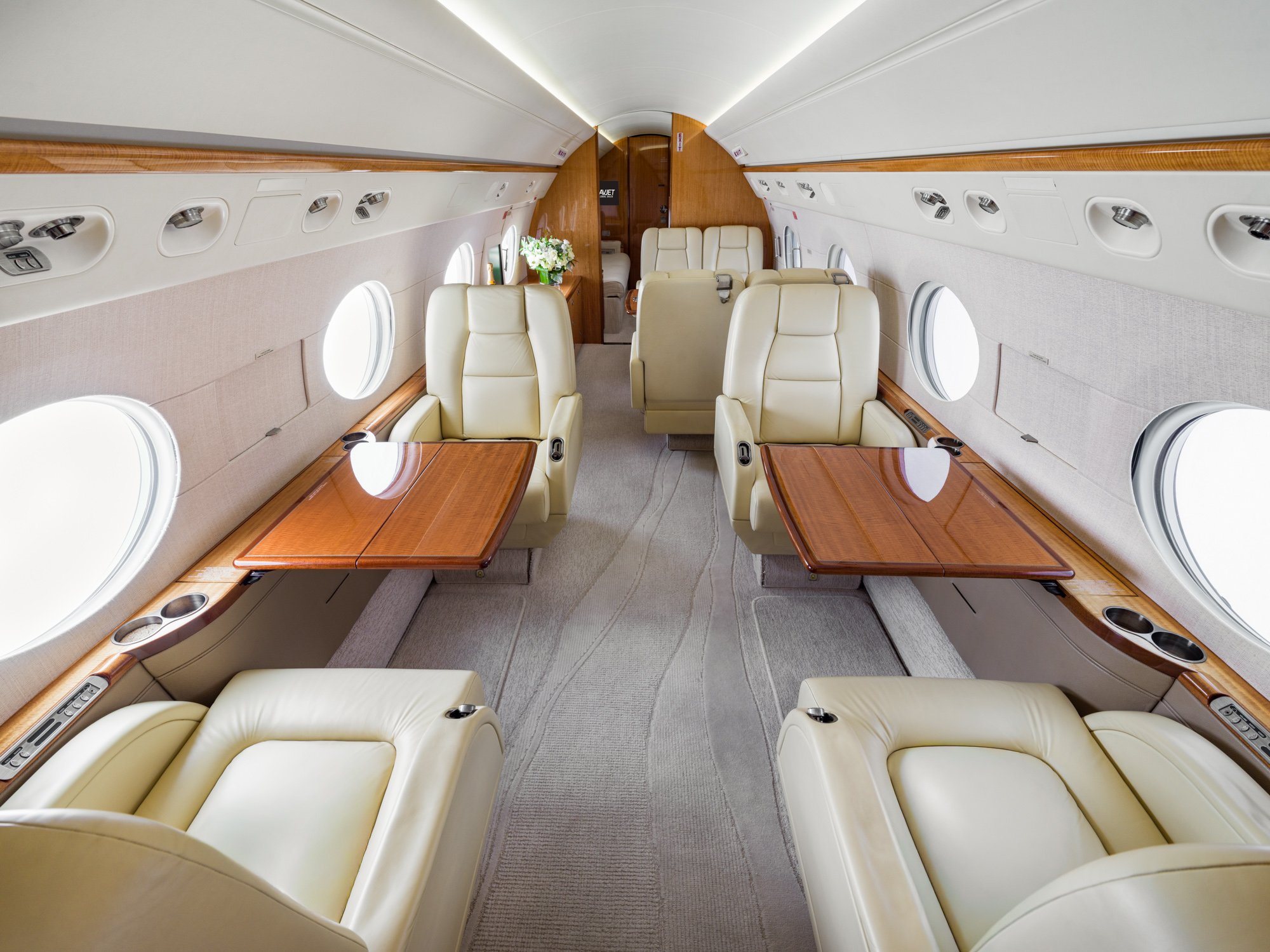 Forward cabin of a Gulfstream 550, view looking aft, featuring four cream leather executive seats with polished wood tables, large panoramic windows, and a spacious aisle—designed for luxury, productivity, and comfort at 40,000 feet.