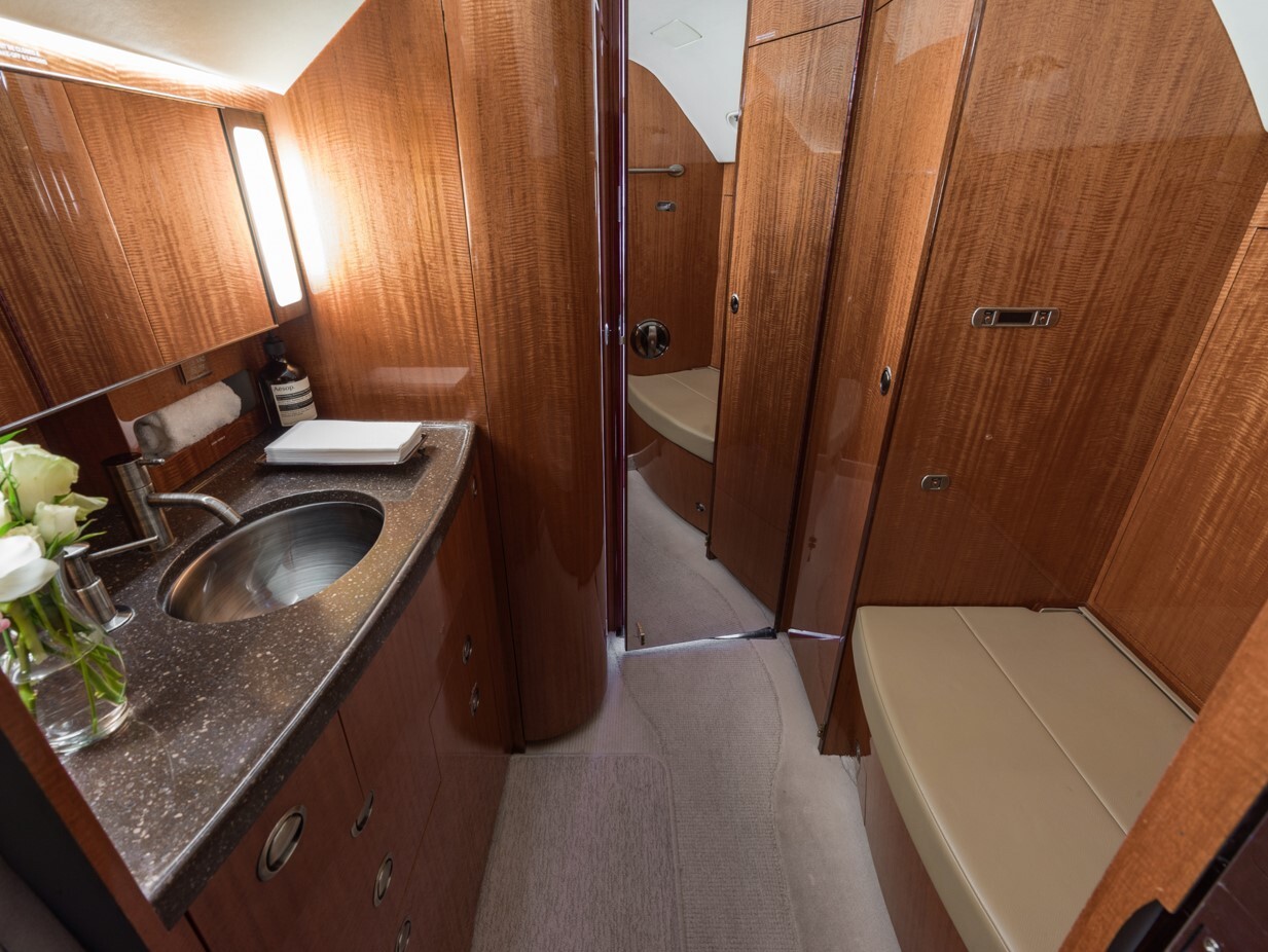 Aft lavatory of a Gulfstream G550, featuring polished wood cabinetry, solid-surface vanity with stainless steel sink, ambient lighting, and integrated seating—designed for elegance, privacy, and in-flight comfort.