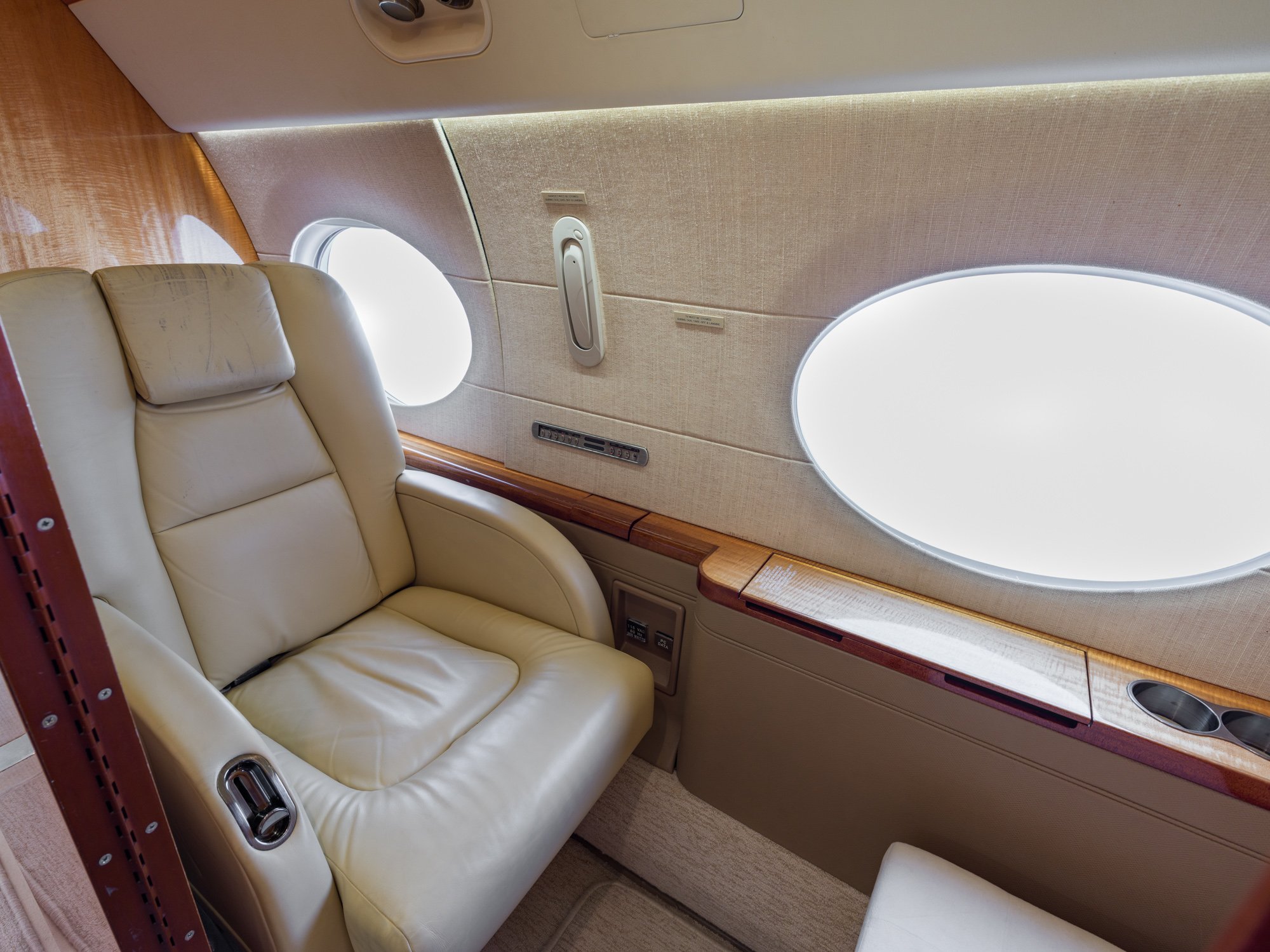 Forward crew rest seat in a Gulfstream G550, featuring a plush leather recliner positioned beside signature oval windows and integrated storage—providing a private, comfortable space for pilot or crew rest during extended flights.