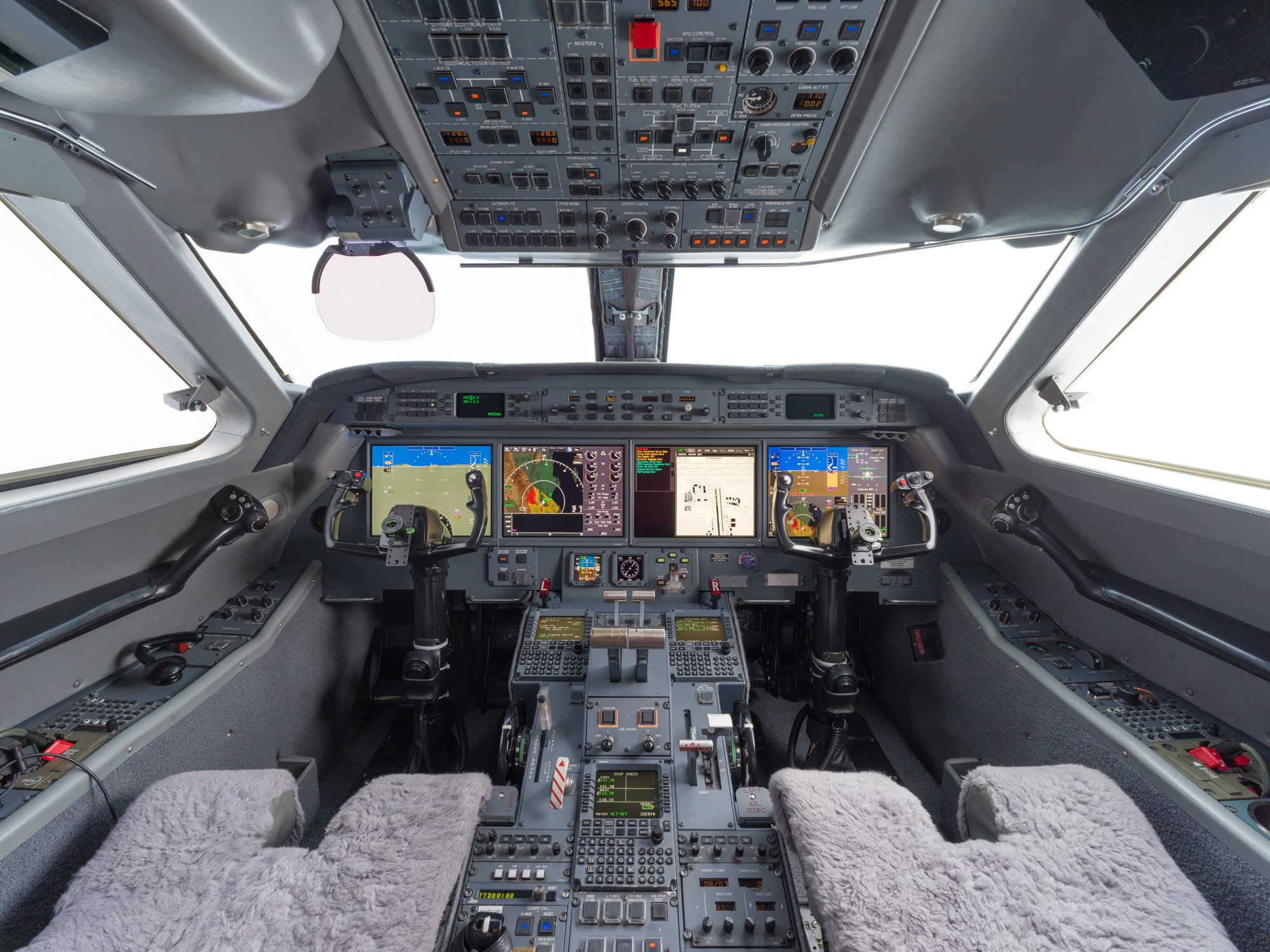 Flight deck of a Gulfstream G550, featuring a dual-control cockpit with advanced avionics suite, four large display screens, overhead switch panels, and plush sheepskin crew seats—designed for precision, safety, and long-range operational performance.