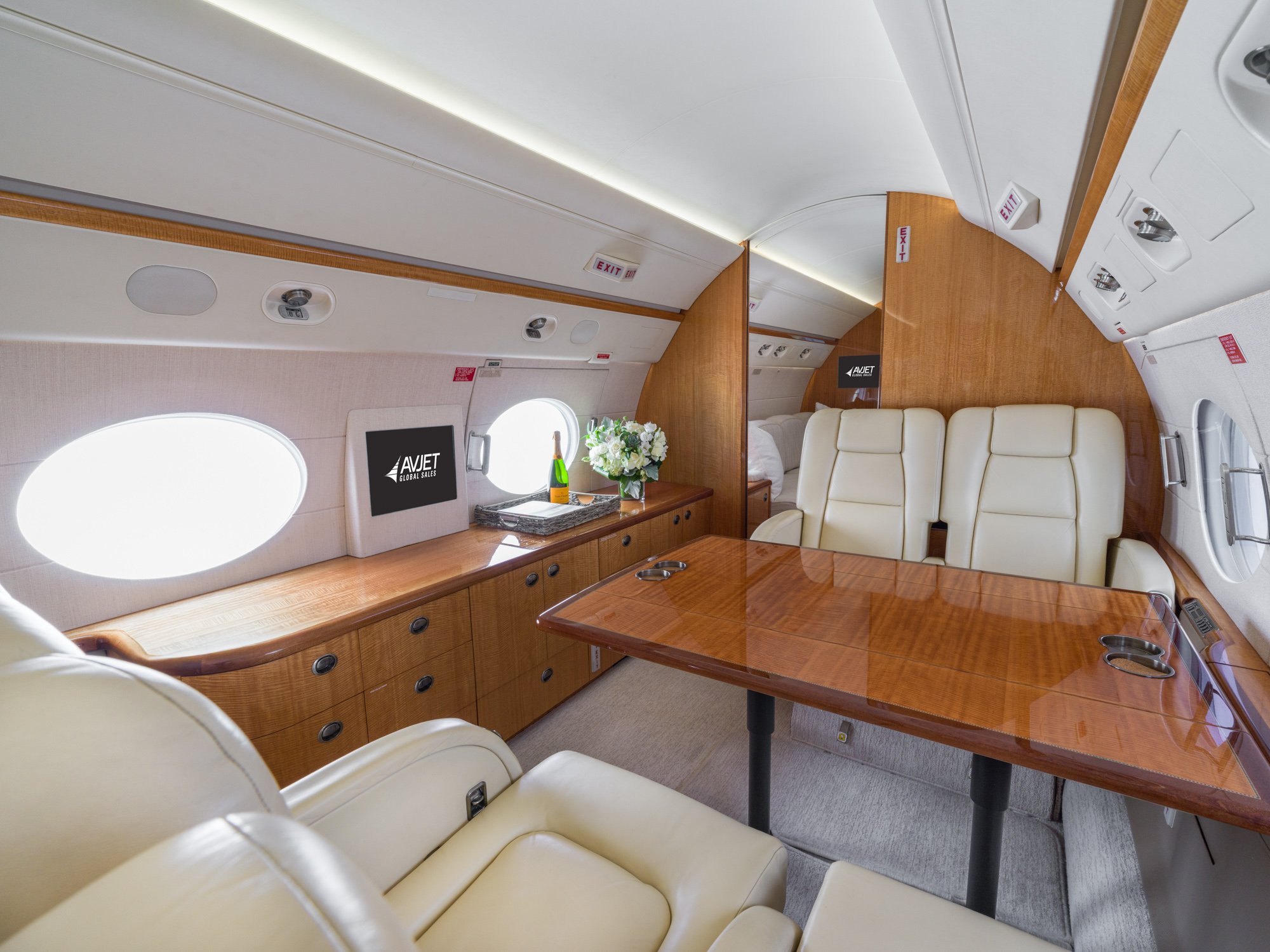 Mid cabin of a Gulfstream 550, view looking aft, showcasing two cream leather club seats with a high-gloss wood conference table, credenza with storage, large panoramic windows, and access to the aft stateroom—designed for productivity, elegance, and uninterrupted long-range travel.