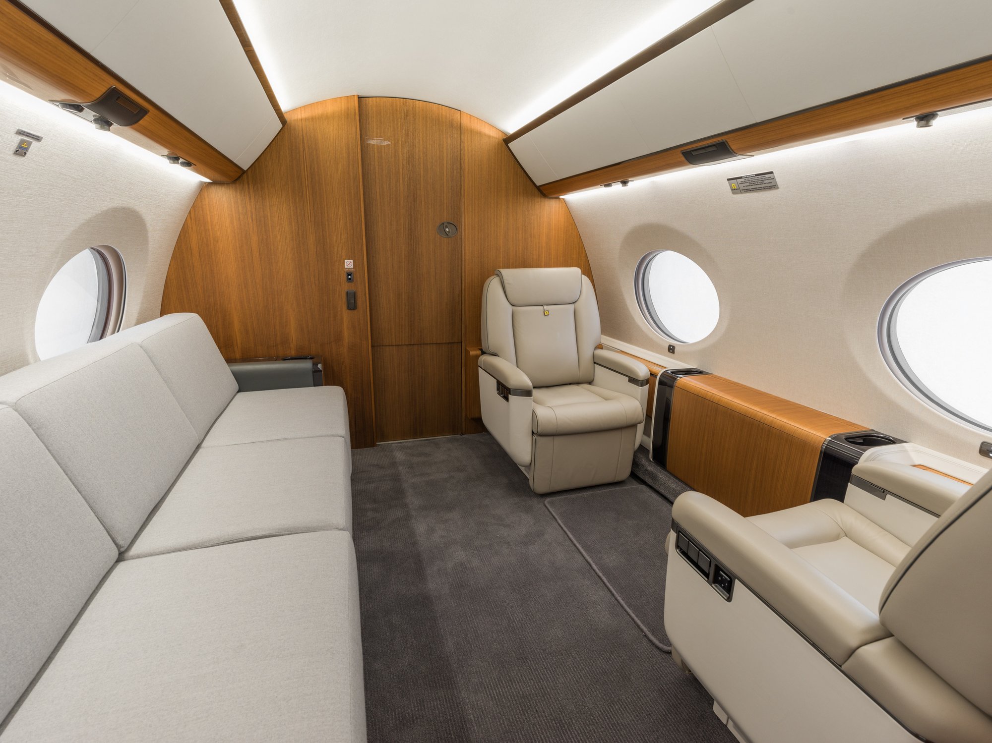 Spacious aft cabin of the Gulfstream 650ER featuring a plush three-seat couch and two facing leather seats, offering comfort and flexibility for private jet travelers.