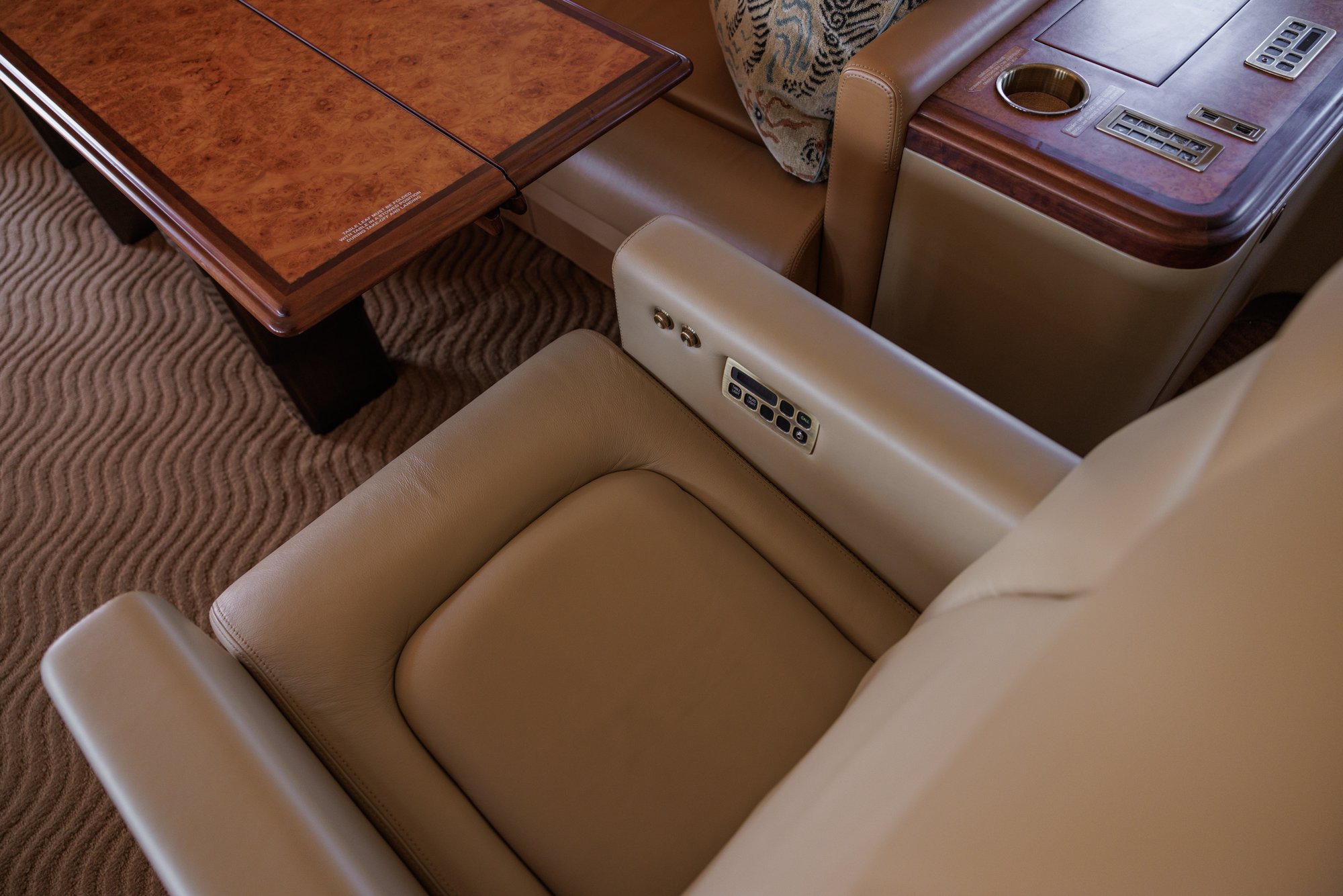 Detail of a leather executive seat in the 2002 Boeing Business Jet 2, featuring integrated electronic controls, premium wood side table, and high-end cabin finish for ultimate passenger comfort.