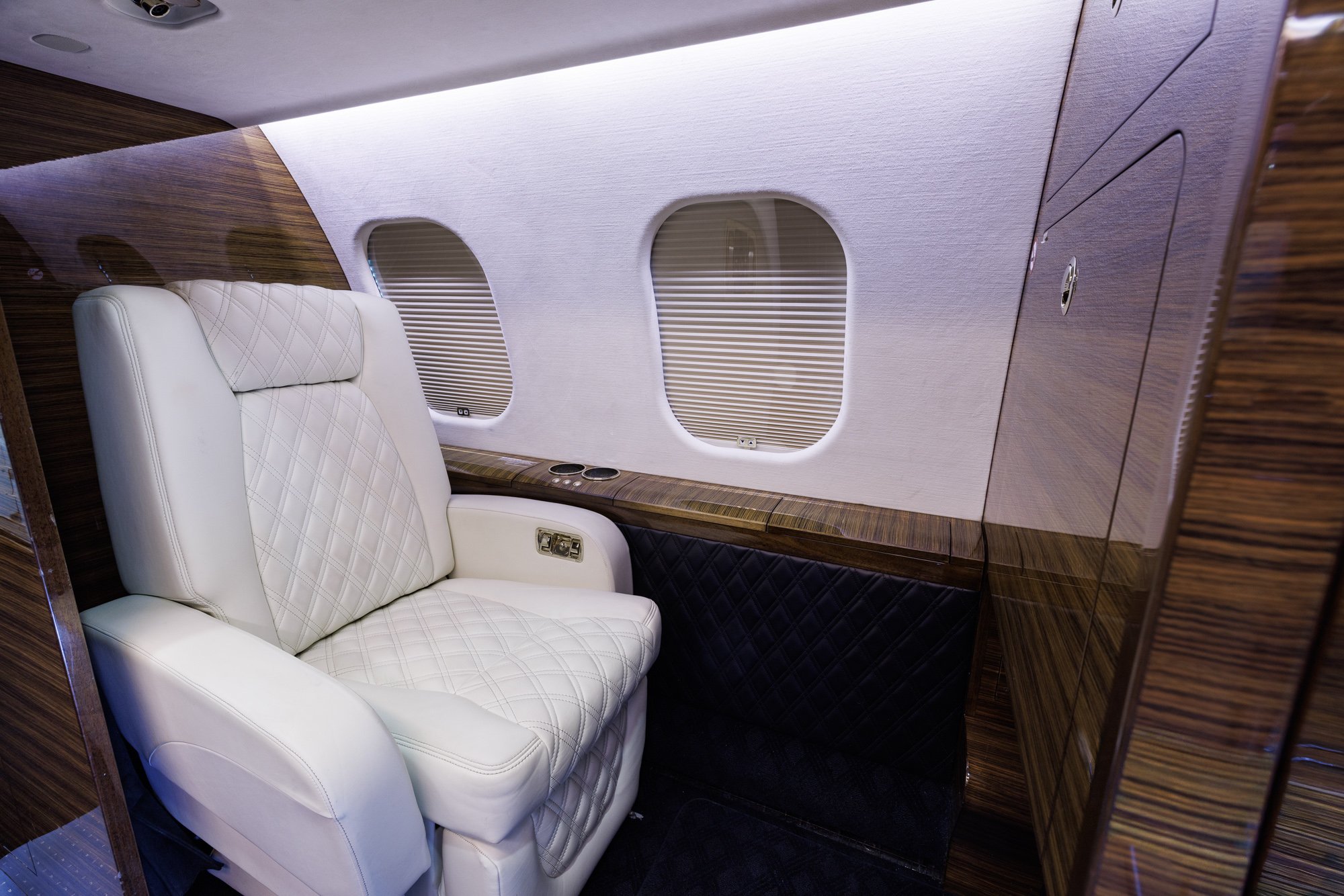 Forward crew rest area inside a Bombardier Global private jet, featuring a diamond-stitched leather reclining seat, elegant wood paneling, and window shades designed for crew comfort during long-range operations.