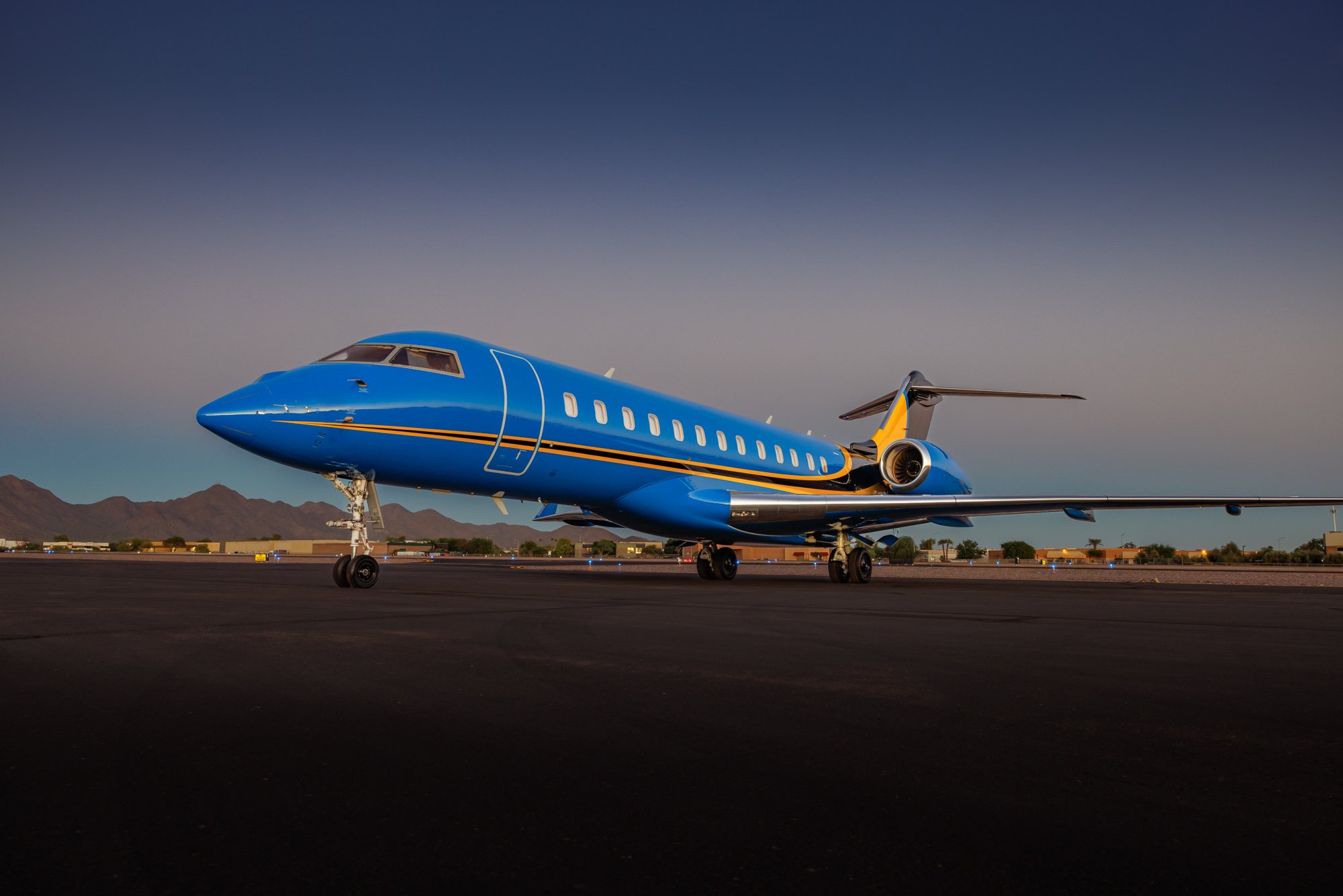 Bombardier Global Express XRS ultra long-range large-cabin private jet with custom blue and gold livery parked on an executive airport ramp at sunset, high-performance business aircraft built for intercontinental corporate travel and global private aviation.