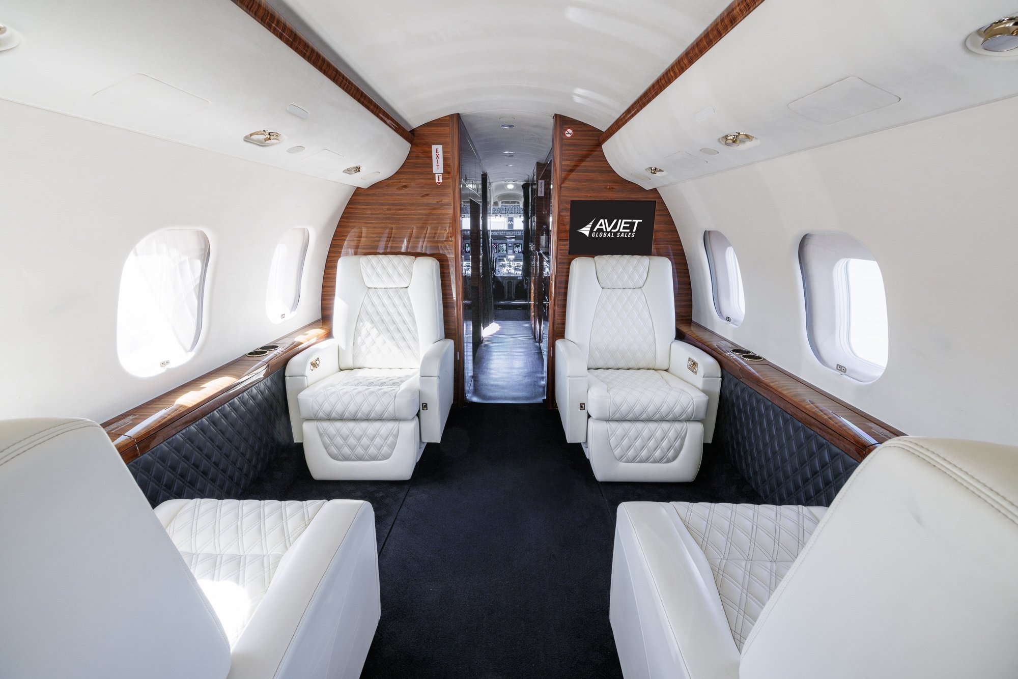 Luxurious Bombardier Global private jet interior featuring white diamond-stitched leather seats, rich wood accents, and spacious cabin layout — designed for comfort, privacy, and long-range travel.