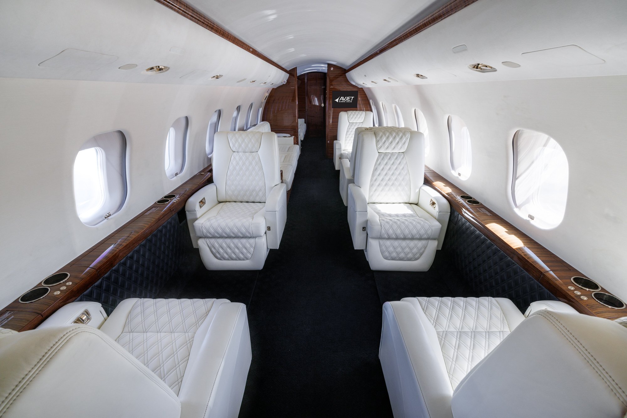 Forward cabin view looking aft inside a Bombardier Global private jet, featuring eight white diamond-stitched leather seats, elegant wood accents, and spacious layout designed for luxury and long-range comfort.