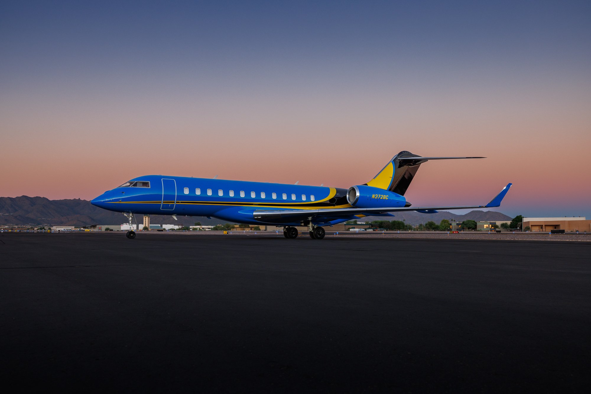 Bombardier Global Express XRS ultra long-range large-cabin private jet with custom blue and yellow livery parked on an executive airport ramp at sunset, premium business aircraft built for intercontinental corporate travel and global private aviation.