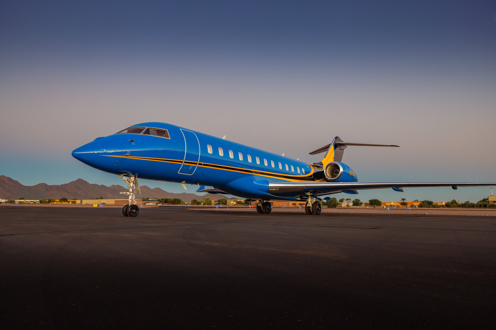 Bombardier Global private jet in custom blue and yellow livery parked on the tarmac at sunset, highlighting its sleek design, long-range performance, and luxury craftsmanship.