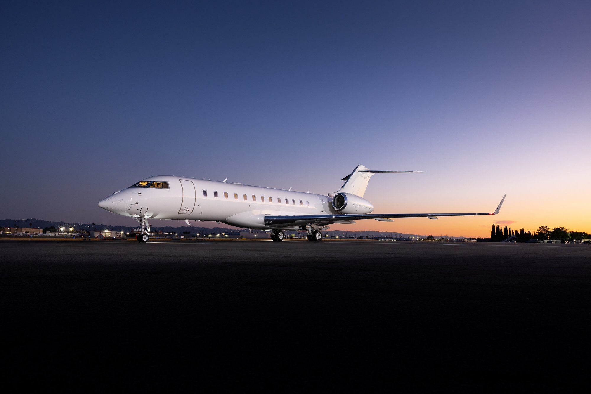 2007 Bombardier Global XRS private jet photographed at sunset on an airport runway, highlighting its distinctive long-range aircraft design, sleek white exterior, rear-mounted engines, and refined executive aviation profile.