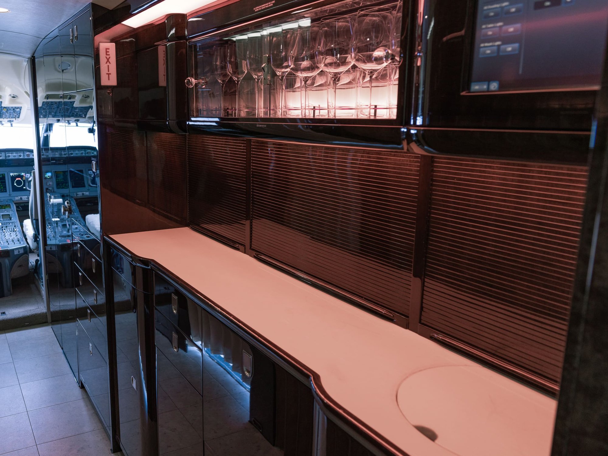 The Galley & Bar Area of the 2007 Bombardier Global XRS features elegant dark wood cabinetry, a spacious serving counter, and illuminated glassware storage. Designed for premium in-flight service, this sophisticated area combines functionality with the refined style of a luxury private jet.