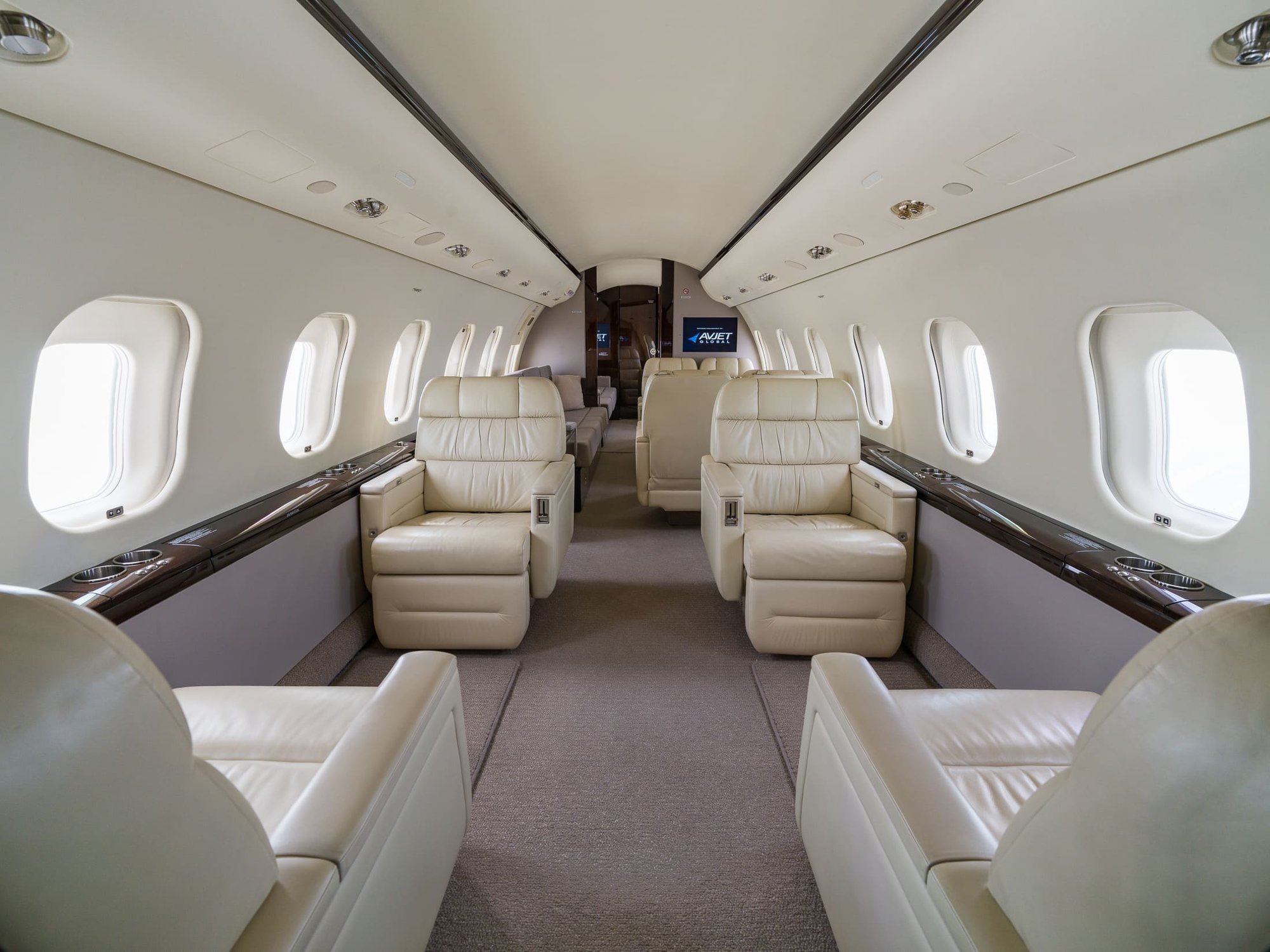uxurious 2007 Bombardier Global XRS private jet interior featuring spacious cream leather executive seating, elegant wood accents, individual windows, ample storage, and a refined cabin layout designed for comfort and long-range business travel.