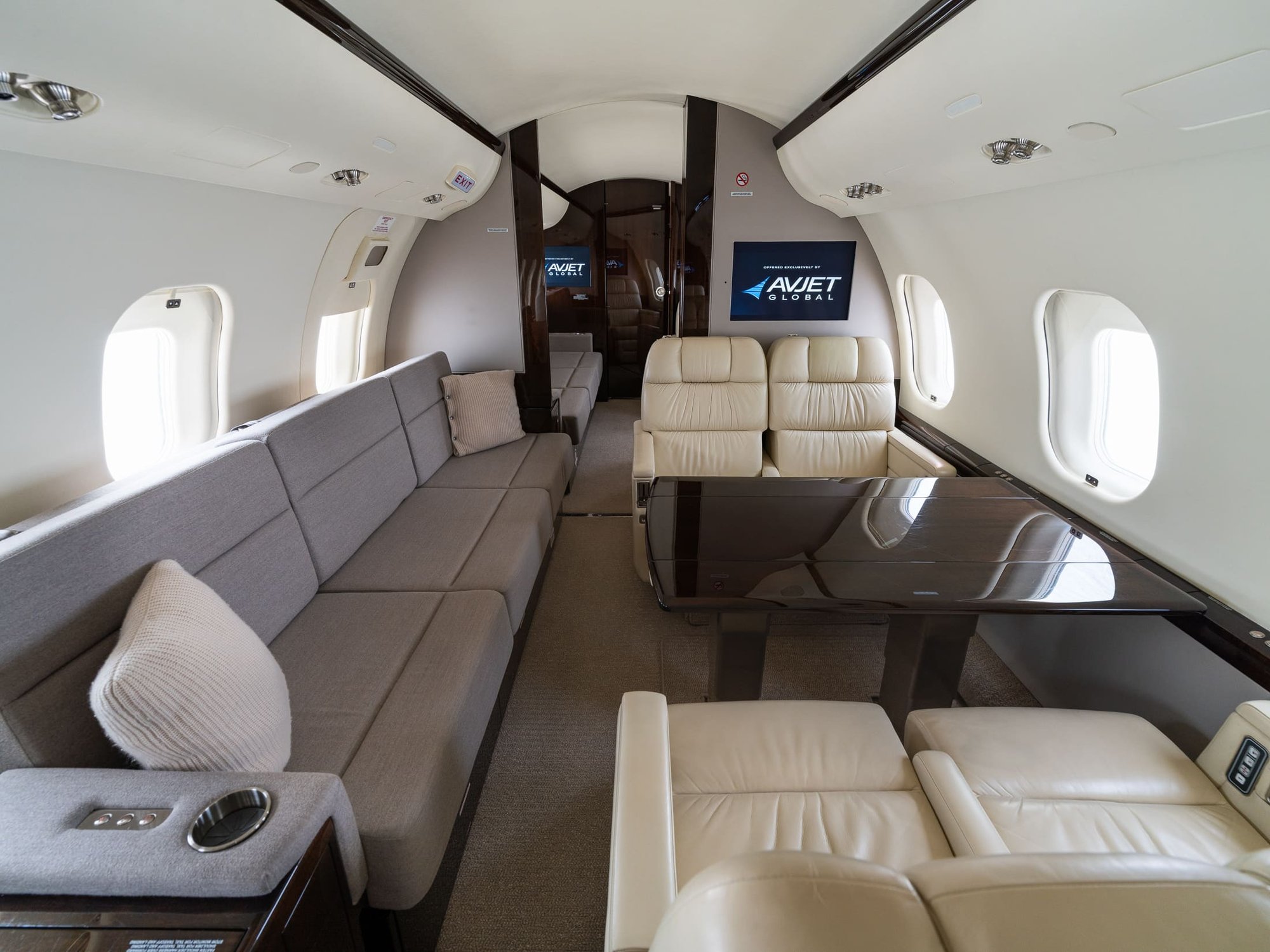 Elegant 2007 Bombardier Global XRS private jet cabin featuring premium cream leather club seating, a spacious side-facing sofa, polished wood dining table, individual passenger windows, and sophisticated executive finishes designed for luxury and comfort.