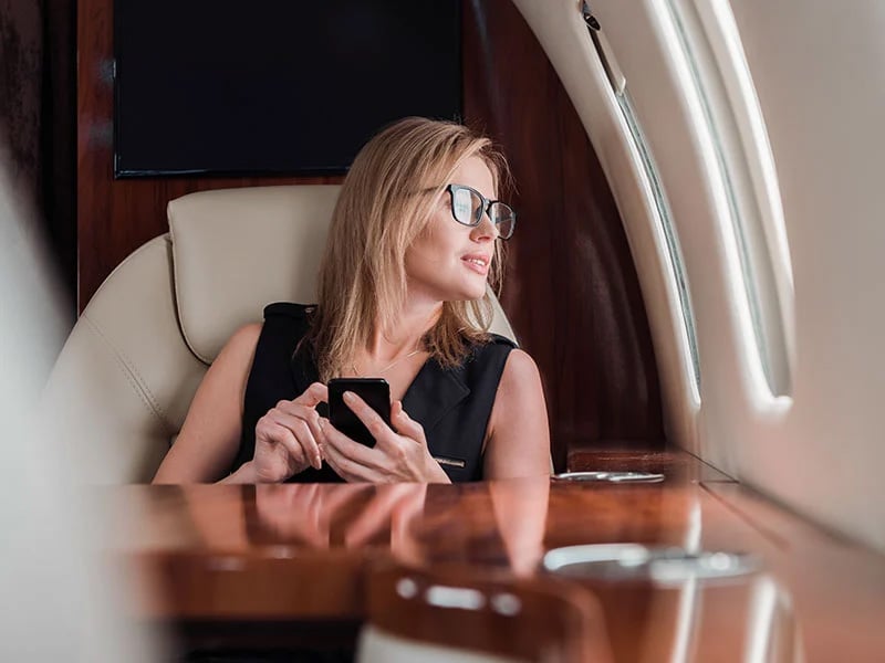 Businesswoman in glasses holding smartphone in private jet